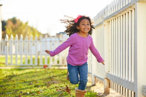 little girl running in a backyard with white picket fence enclosed