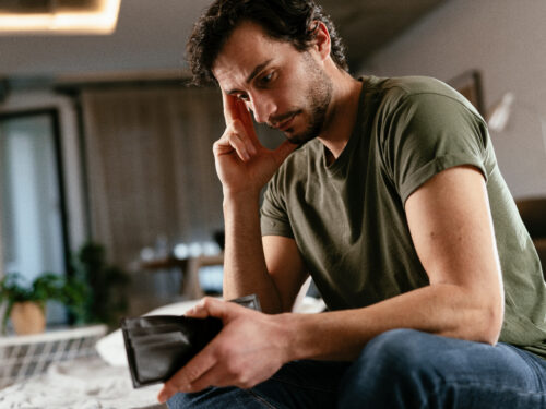 Unemployed sad man sitting at home showing empty wallet
