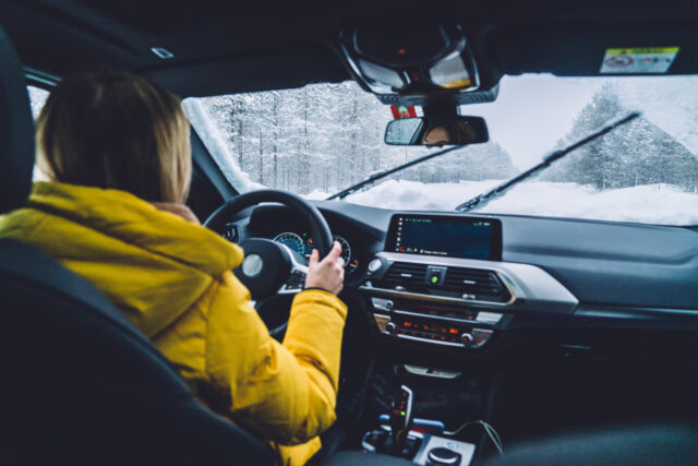 Cropped image of woman holding hands on helm driving on snowy offroad in wood during expedition, female traveling by car
