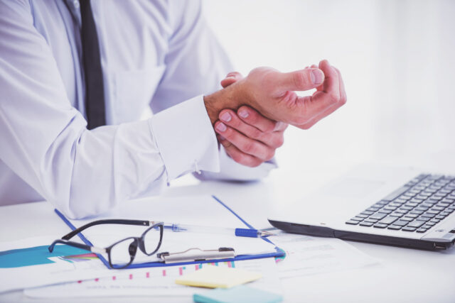 Illness hand. Portrait of a businessman while working in his office, holding hand