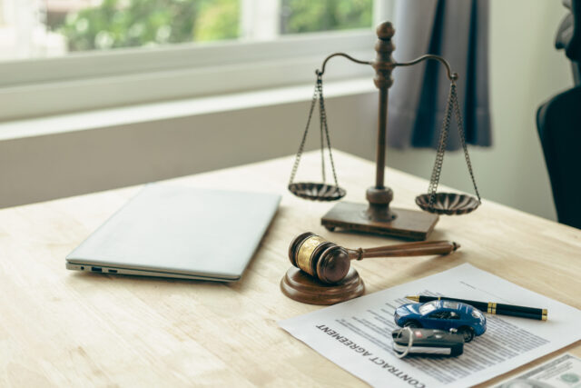 A wooden desk holds a closed laptop, a set of scales symbolizing justice, a gavel, a 