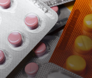 Close-up of blister packs containing round, pink and yellow tablets. The packs are partially overlapping, highlighting different textures and transparent sections that reveal the color and shape of the pills, while alerting to the presence of a potentially defective drug.