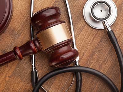 A wooden gavel and a stethoscope are placed on a wooden surface, symbolizing the intersection of law and medicine.