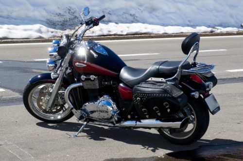 A sleek black and red motorcycle stands proudly on the paved road, showcasing its chrome details and leather saddlebag. The glistening snow lining the roadside creates a striking contrast with this powerful machine.