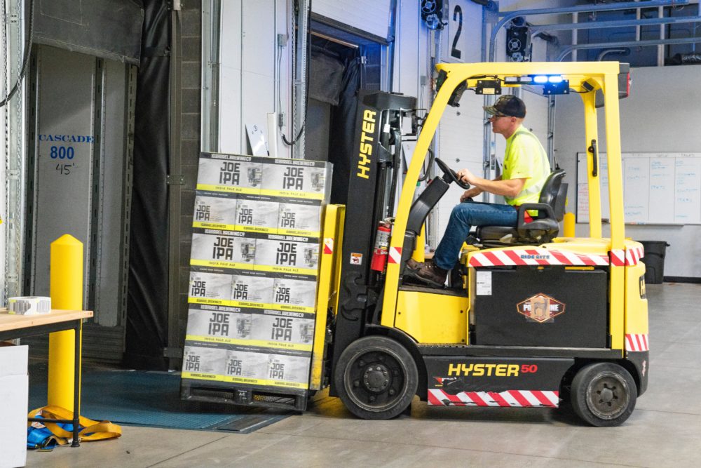 A worker skillfully operates a yellow Hyster 50 forklift, maneuvering a pallet loaded with 