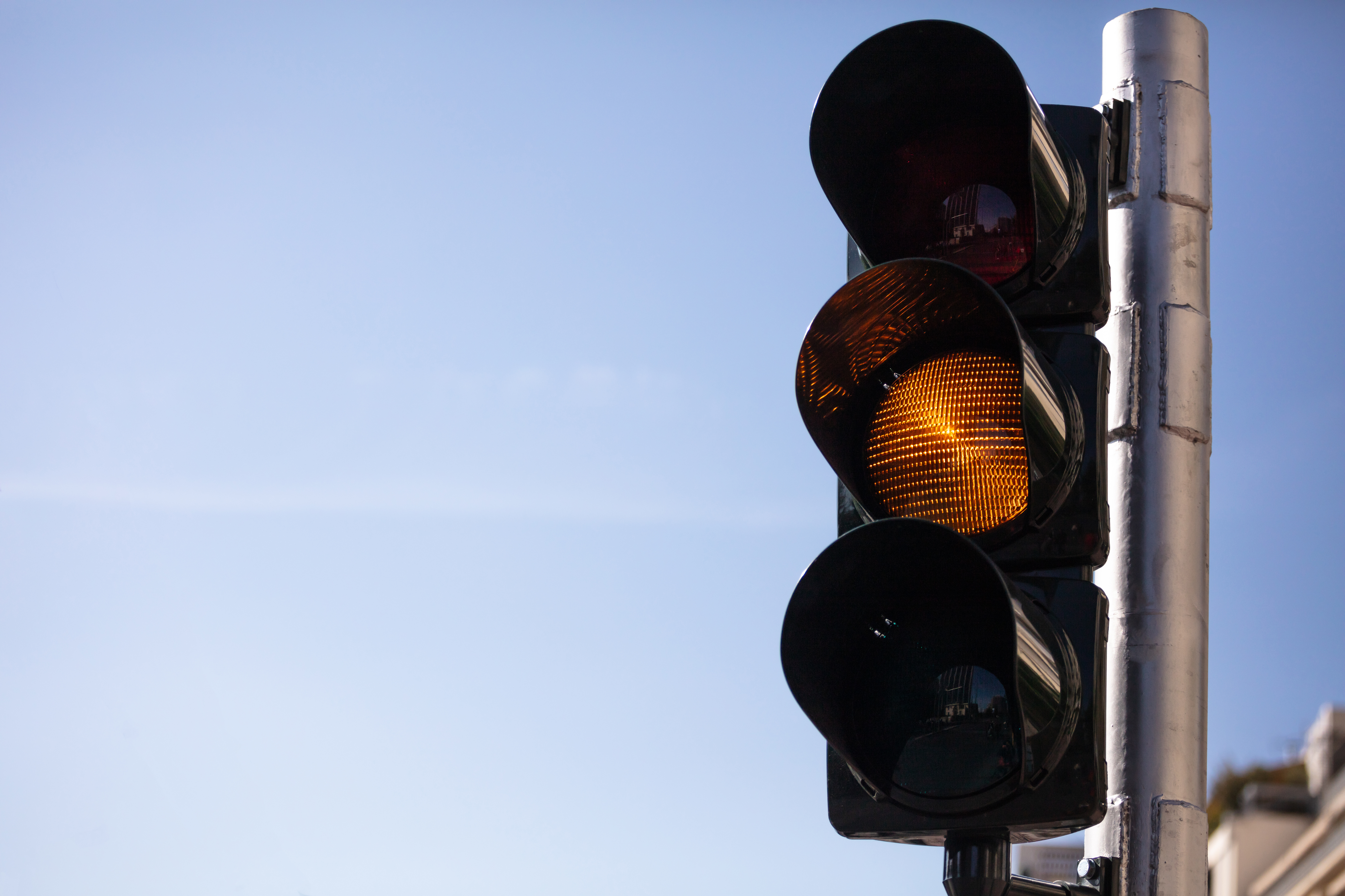 A traffic light set against a clear blue sky displays a yellow light, indicating caution. The metal structure holds three circular lamps, with the yellow light illuminated in the center—a reminder of how faulty traffic signals can prompt extra vigilance.