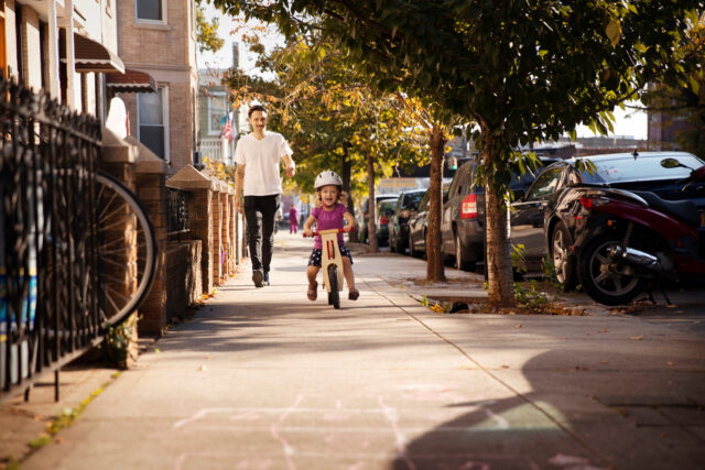 person walking on sidewalk with child on bike