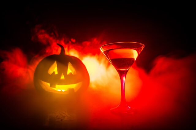 Halloween pumpkin orange cocktails. Festive drink. Halloween party. Funny Pumpkin with a glowing cocktail glass on a dark toned foggy background.